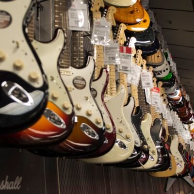 Row of colorful electric guitars hanging in a music store, showcasing diverse models and prices.